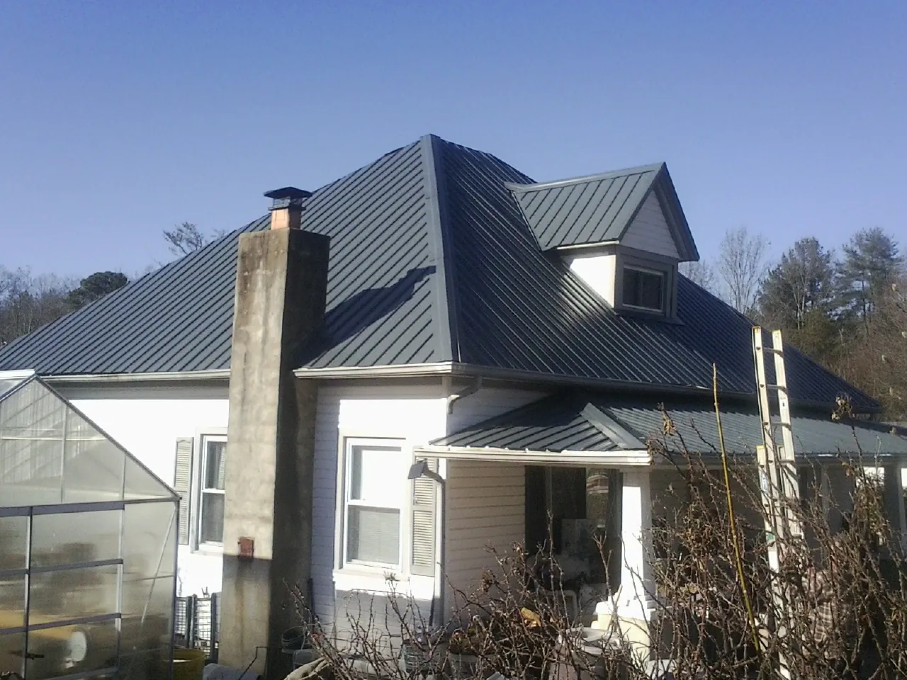 Dark blue standing seam metal roof on a white farmhouse with dormer — Slate & Tile Roof Repair by Roofing Brothers in Delanson