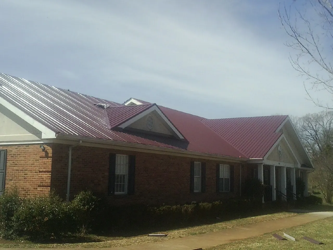 Red metal roof with gabled entries on a long brick building, from a Hail Damage Roof Repair job in Delanson