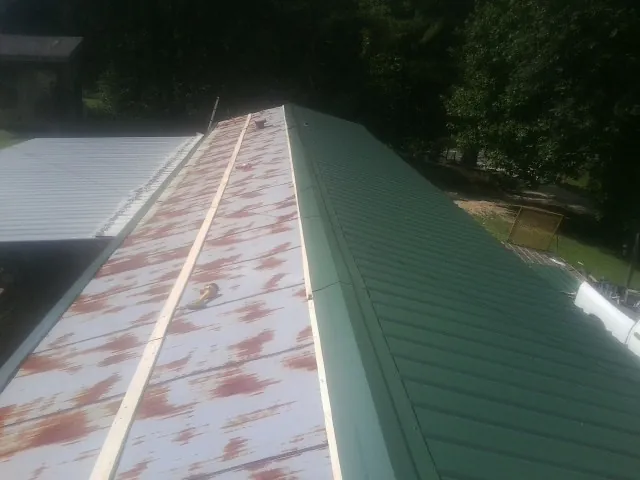 Old rusted panels beside newly installed green metal roofing — Wind Damage Roof Repair by Roofing Brothers in Delanson