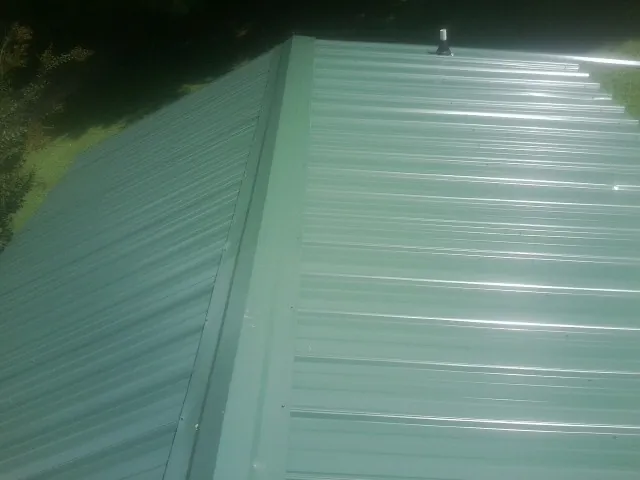 New green metal panels meeting at the ridge of a roof — Flat Roof Repair work by our crew in Delanson