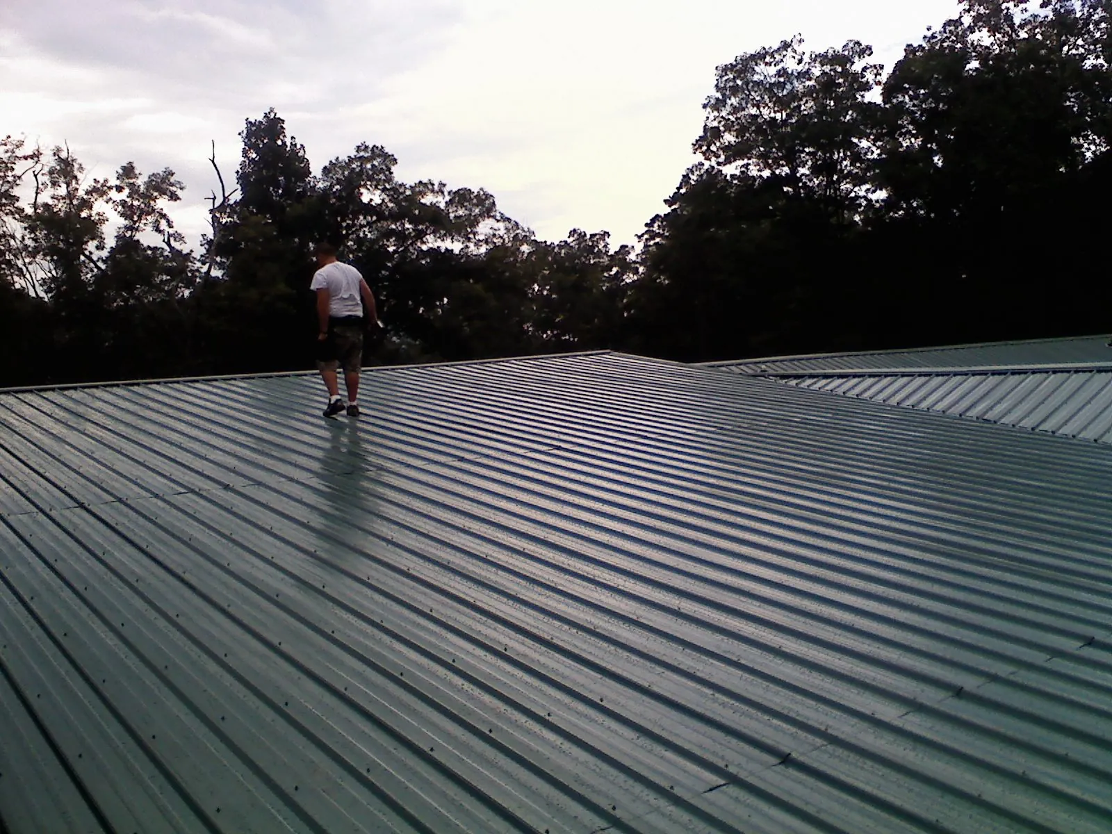 Roofer walking a wide expanse of new green metal roofing in Delanson