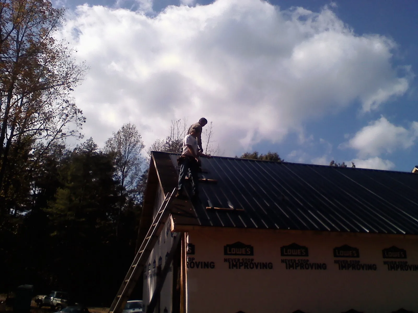 Roofer fastening dark metal panels high against a cloudy sky, from a Roof Inspection job in Delanson