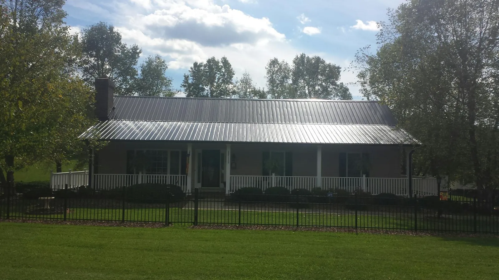 Gray metal roof on a brick ranch with a full width front porch — Gutter Guard Installation work by our crew in Delanson