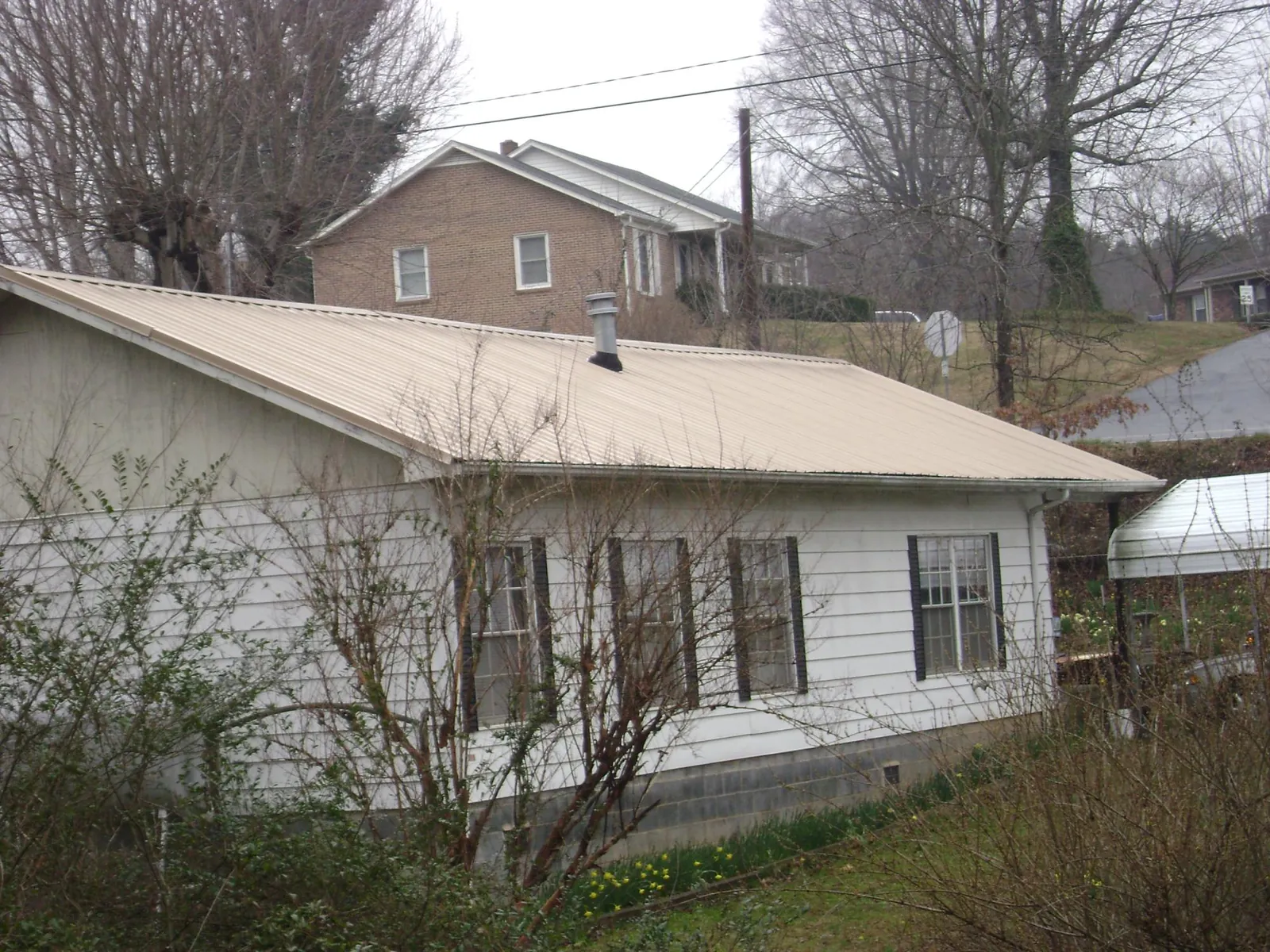 Tan metal roof on a white sided house set into a hillside — Commercial Roofing by Roofing Brothers in Delanson