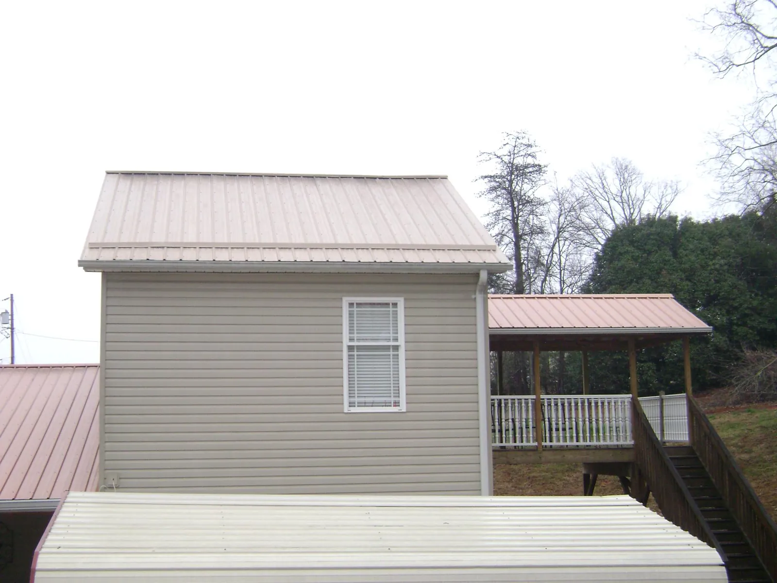 Tan metal roofs on a two story addition and attached porch, from a Roof Replacement job in Delanson