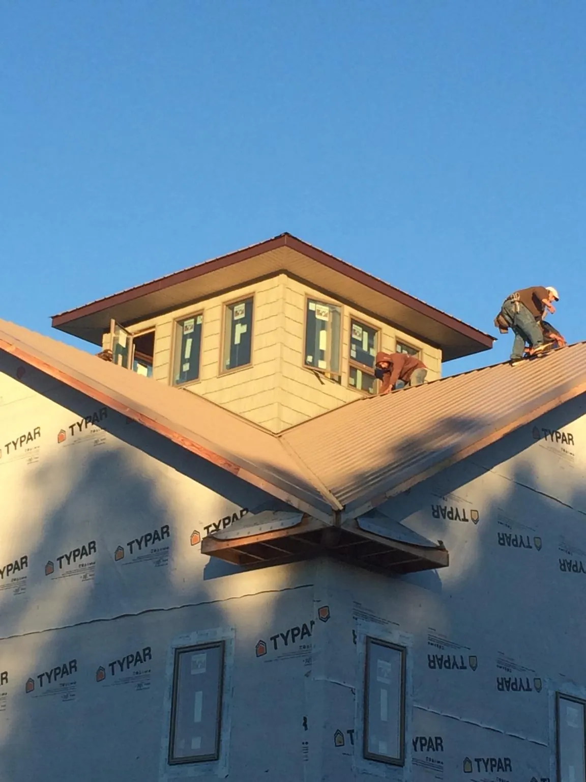Roofers working around a rooftop cupola on a new metal roof at sunset — Roof Waterproofing in Delanson by Roofing Brothers